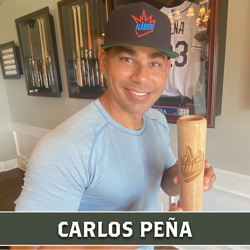 Carlos Peña smiling and holding a wooden baseball bat-shaped container with the Plakata logo, with his name displayed in a banner at the bottom.