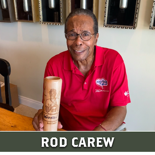 Rod Carew smiling and holding a wooden Dugout Mugs baseball bat mug engraved with a portrait.